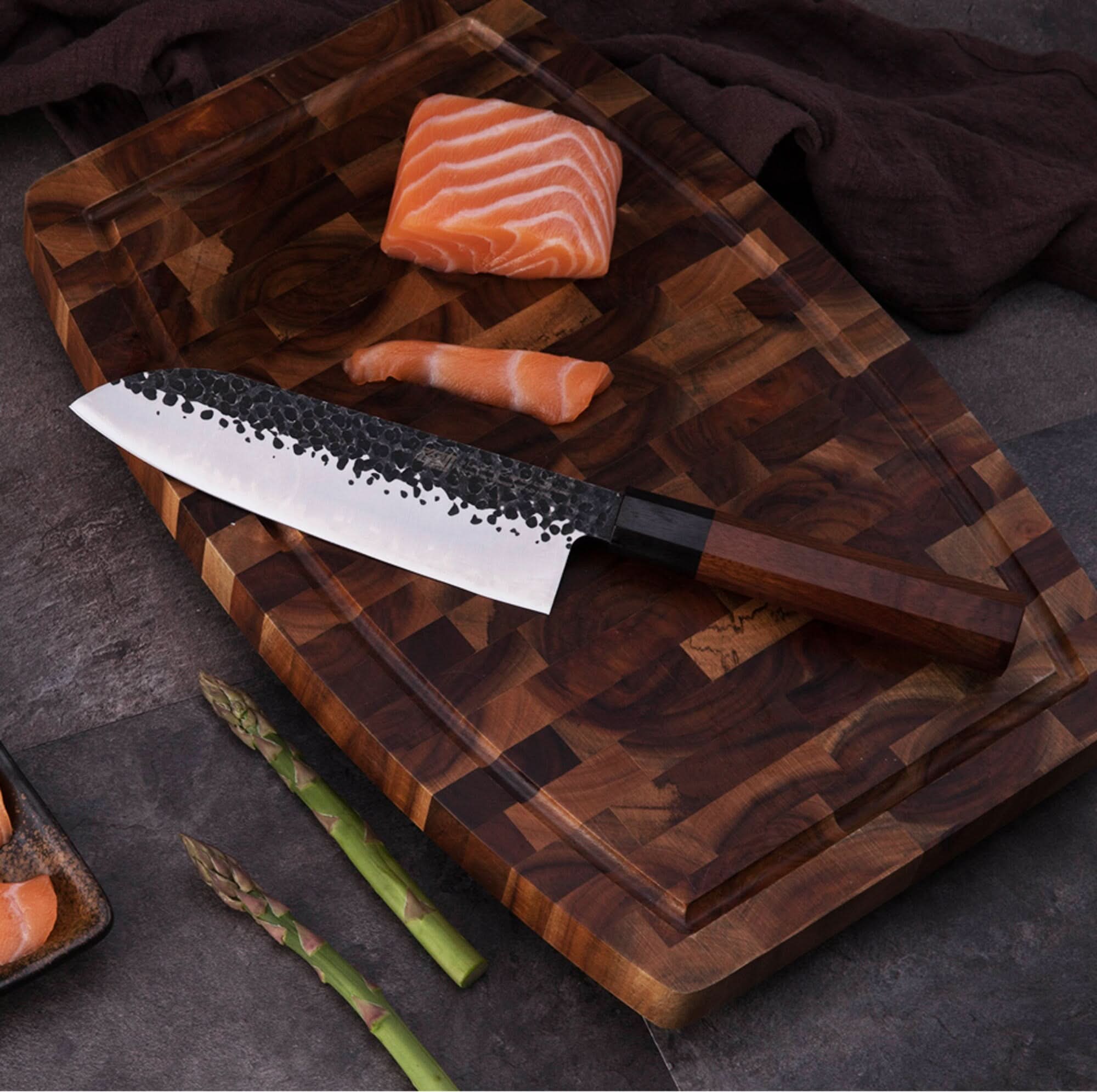 Japanese Forged Knife with hammered steel blade on wooden cutting board with salmon and asparagus.